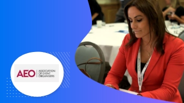 A woman in a red blazer is sitting at a table with a white tablecloth and AEO logo.