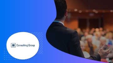 A man in a suit is giving a presentation at a conference for the AK Consulting Group.