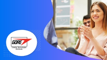 Gore Associates with a smiling woman and a man sitting in a green outdoor area.