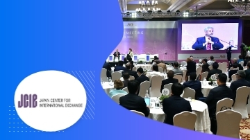 Group of people sitting in a room with a big screen at the front showing a man.