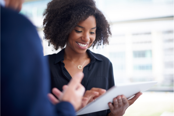 Woman with tablet smiling while a man shows her something on his tablet.