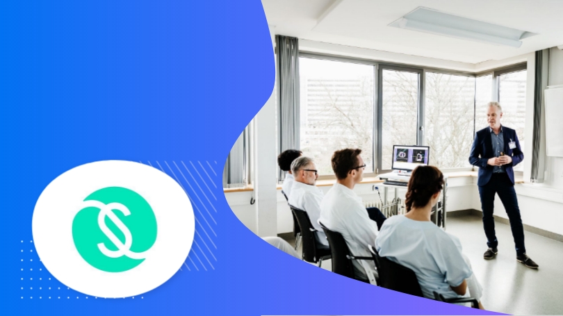Group of people in a meeting room with a man speaking, and a dollar sign in the foreground.