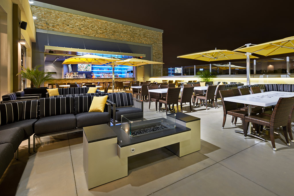 A Houston rooftop bar with an outdoor fireplace, brick walls, cushioned seating, and large yellow umbrellas.