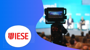 Camera with red logo in front of a large audience with a blue background and text.