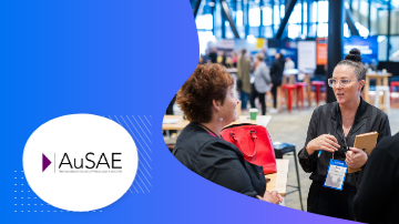 Two women talking in front of the AuSAE logo at a conference.