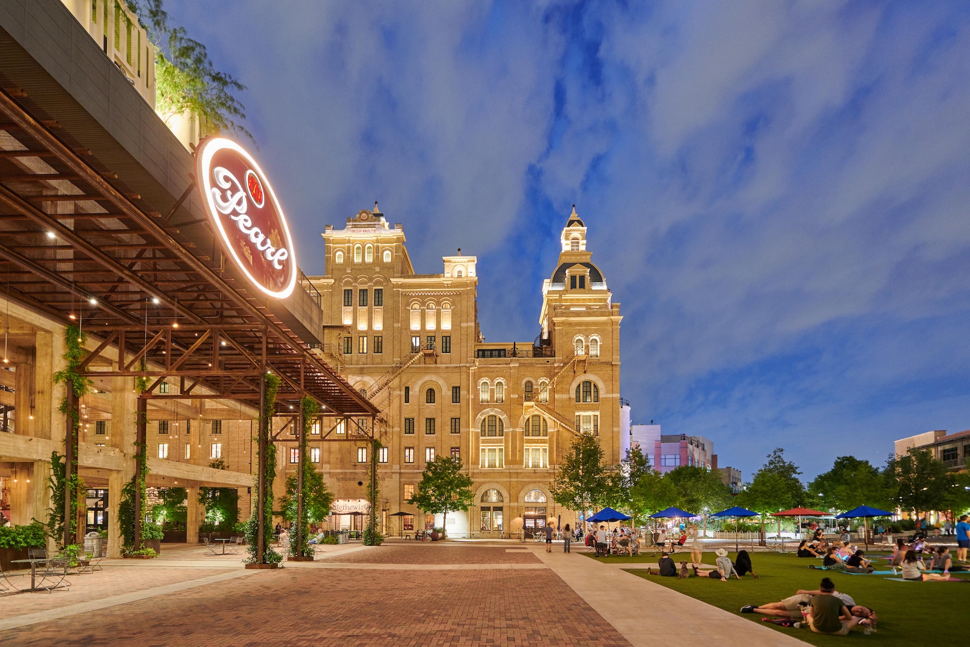 Dusk view of Pearl, with an illuminated sign, architecture, landscaping, and people enjoying the ambiance.