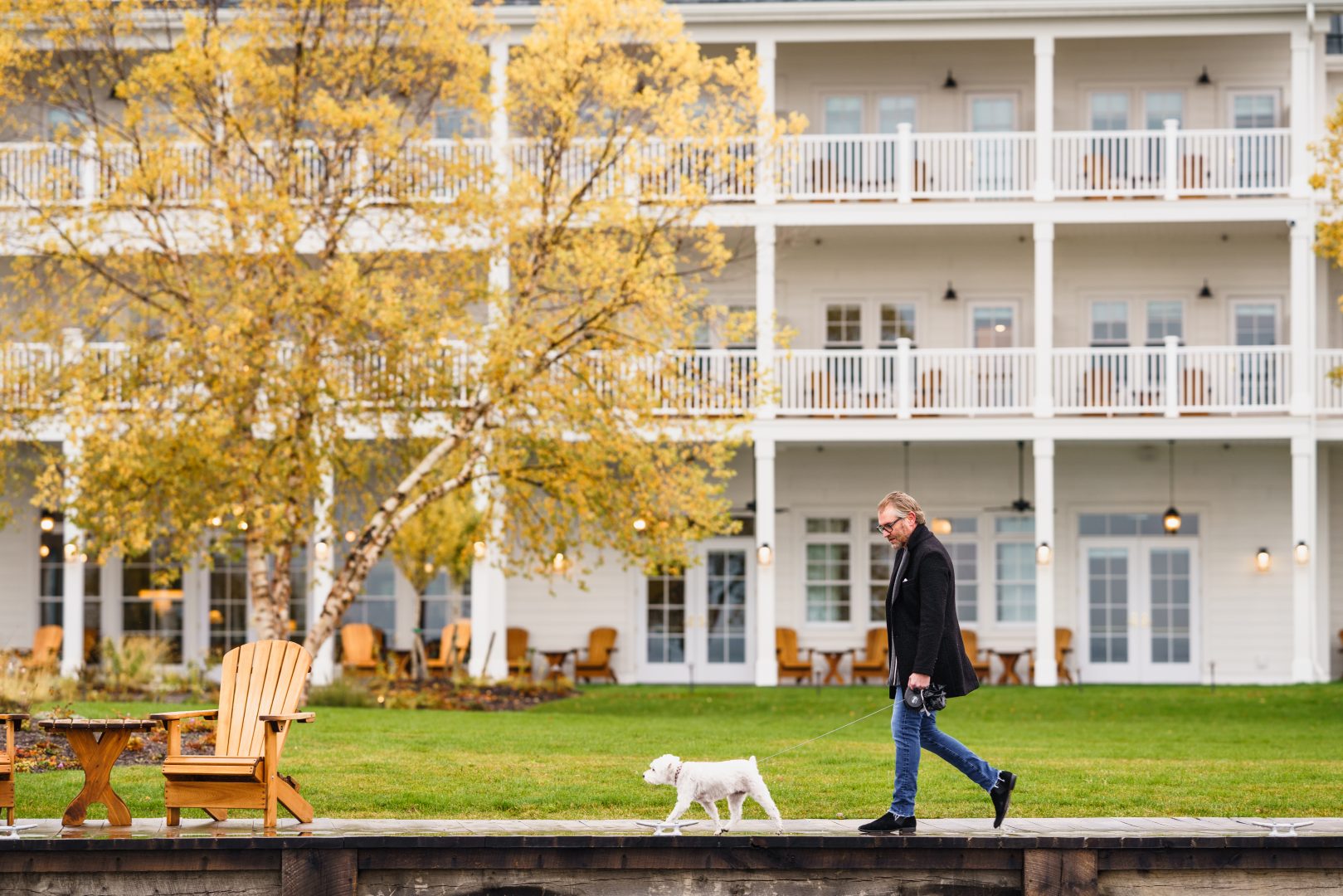 A man walks his dog on a leash past a row of Adirondack chairs at Inn at Bay Harbor.