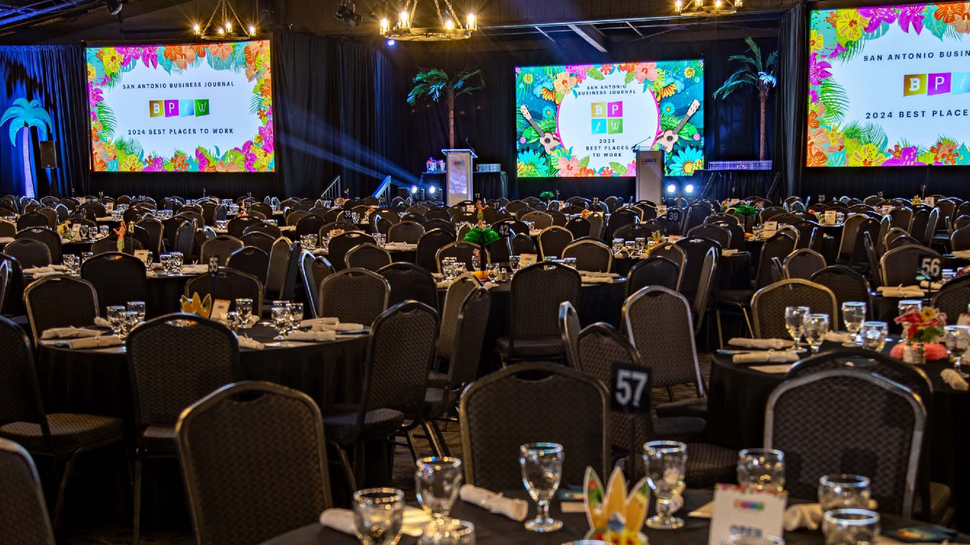 Ballroom at Grand Hyatt San Antonio Riverwalk with tables set for dinner and three large screens displaying text.