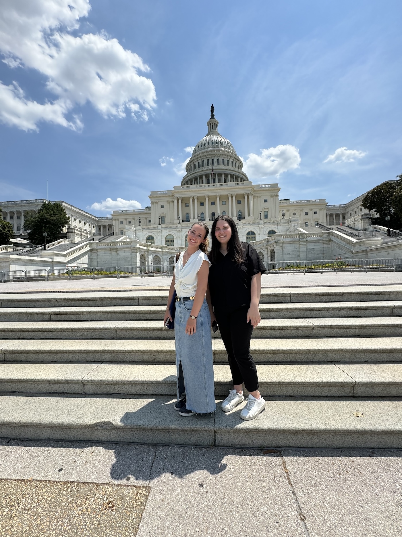 Two women smiling in front of the US Capitol building in Washington, DC, on a sunny day.