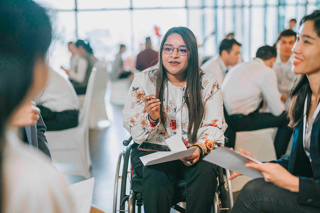 Woman in wheelchair holding papers talks to another woman at an event at the Singapore Marriott Tang Plaza Hotel.