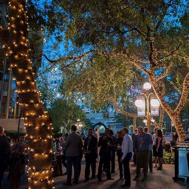 Many people gathered at the center for performing arts at night, with trees and buildings in the background.