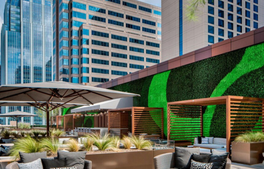 An outdoor seating area with couches, umbrellas, and a green wall in front of tall buildings.