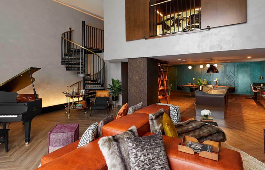 Hutton Suite, a modern interior with orange couches, a piano, and a spiral staircase.
