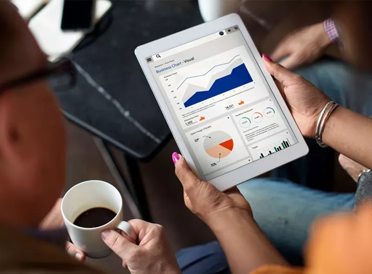 A woman is holding a tablet with a business chart and a cup of coffee.