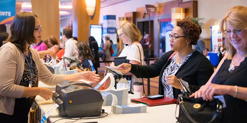 A woman scanning a badge while another woman is smiling and waiting to be scanned.