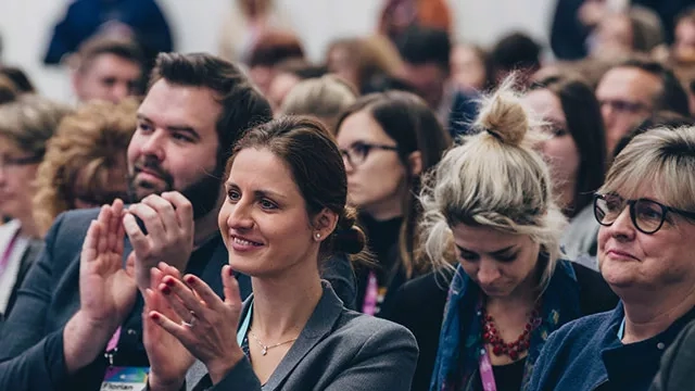 A group of people in a conference room with one woman clapping her hands in the middle.