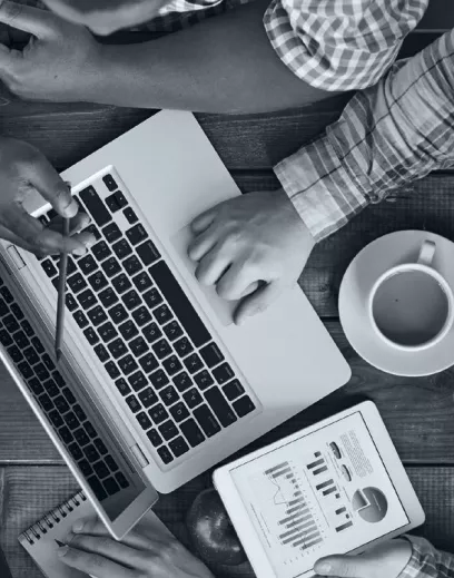 Laptop, tablet, and coffee cup on a desk with hands, symbolizing the importance of digital tools in business.