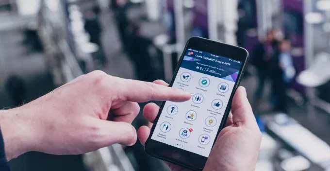 Hands holding a phone with an app opened showing the MELIA logo and some icons.
