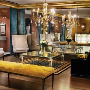 A luxurious room with a glass table, yellow bench, chandeliers, and a mirror wall in a hotel.