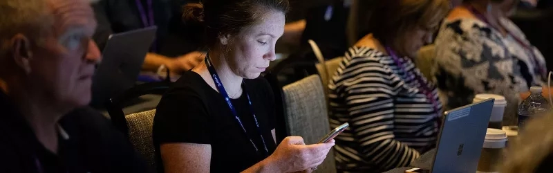 Attendees at a conference using their smartphones while a woman looks at hers.