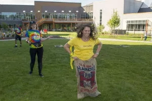 Two girls play sack race on a green field in front of a building.