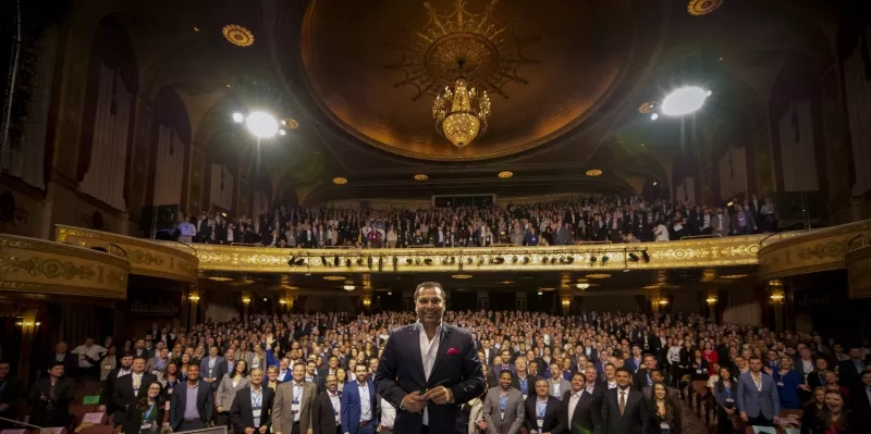 Man stands in front of a crowd of hundreds of people in the Apollo Theater.