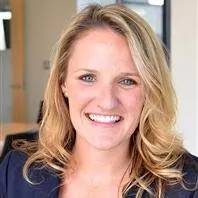 A smiling woman with blonde hair and blue eyes in an office setting.