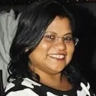 A smiling woman wearing glasses and a black and white dress stands in front of a white dress.