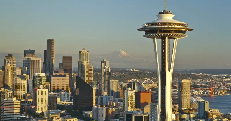 A cityscape of Seattle with many tall buildings and a space needle tower under a clear sky.