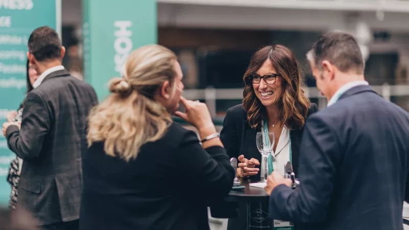 People networking with a blurred background, and one woman is smiling, and the text on the banner is HO.