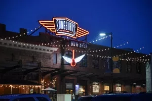 Songbirds neon sign glowing at night with a guitar hanging from it and string lights around the building.