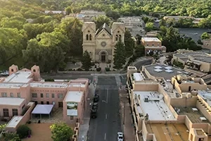 The aerial view of Santa Fe with a cathedral, road, and buildings under a bright sky at dusk.