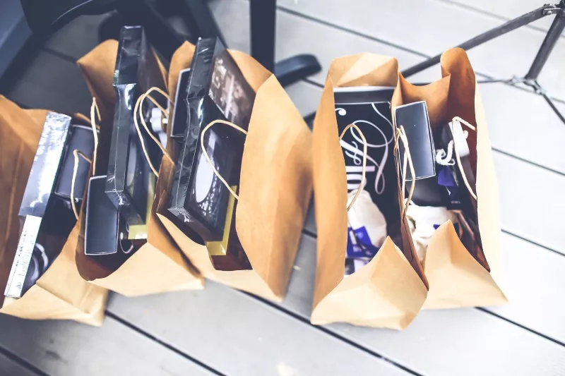 Three brown shopping bags filled with black boxes are placed on a wooden floor from above.
