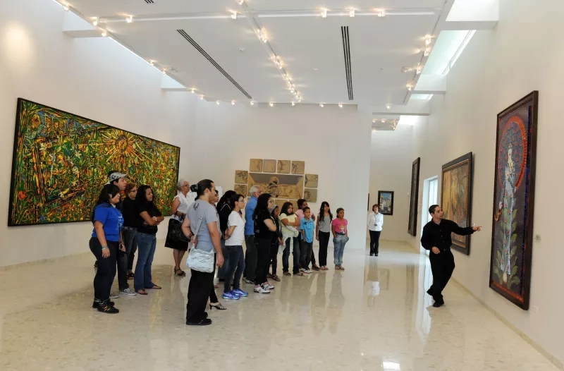 People on a tour in the Museum of Contemporary Art in Puerto Rico, with paintings on the walls.
