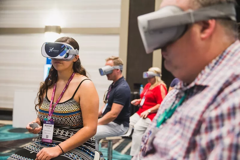 A group of people are sitting in chairs and wearing virtual reality glasses inside the building.