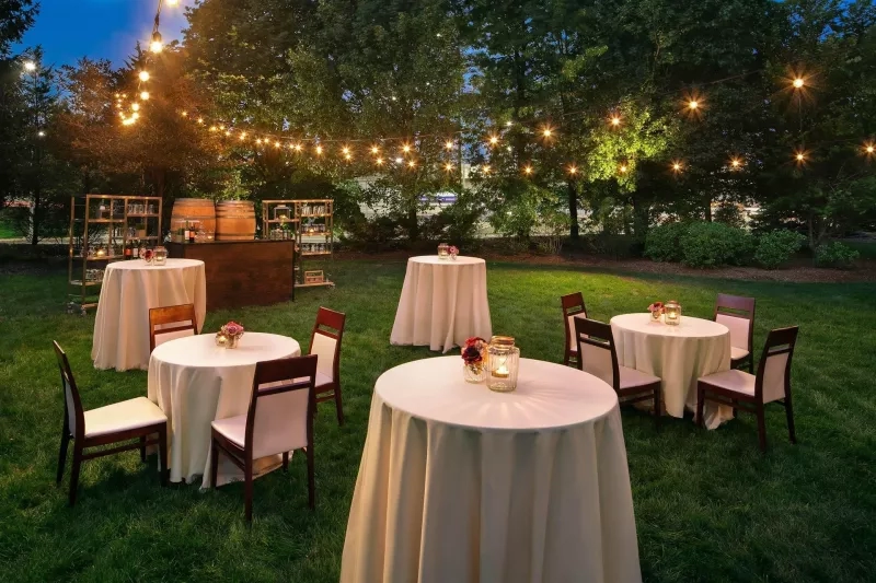 Outdoor wedding reception area with round tables, white tablecloths, string lights, and lush greenery at Hilton Boston Logan.