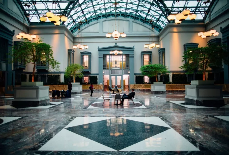People sitting and walking in the lobby of the Chicago Cultural Center with chandeliers and trees.