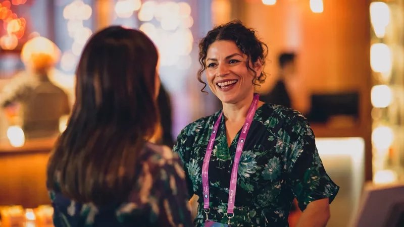 A woman wearing a badge smiles at another woman at the Cvent CONNECT conference.