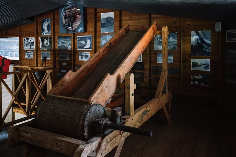 Wooden coffee processing machinery in a museum with walls lined with old black and white photographs.