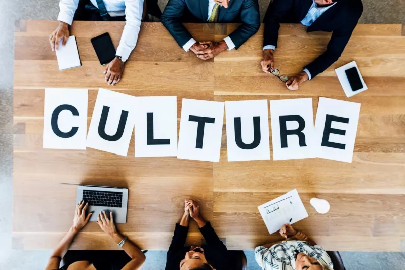 Group of people around a table with the word culture made of paper letters in front of them.