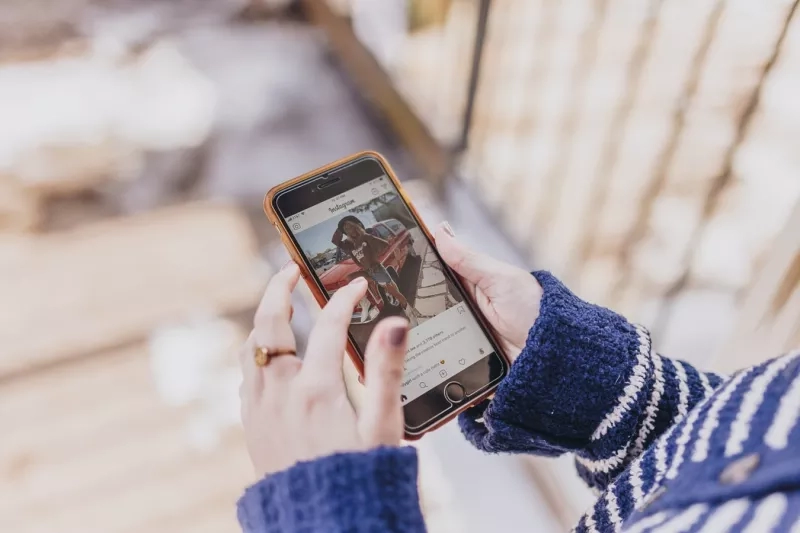 Close up of hands holding a phone with an Instagram post on screen in winter.