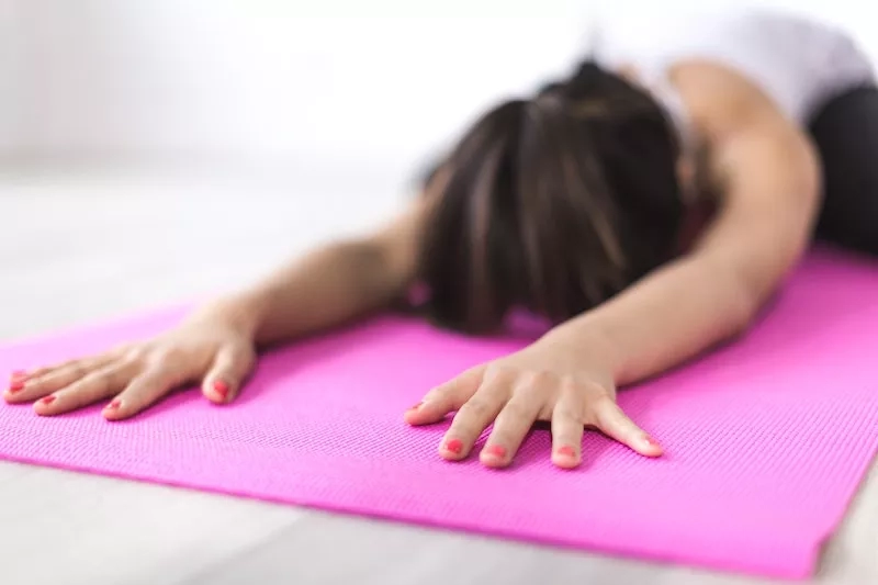 Woman practicing yoga on pink mat with hands on floor and head facing down to floor for exercise.
