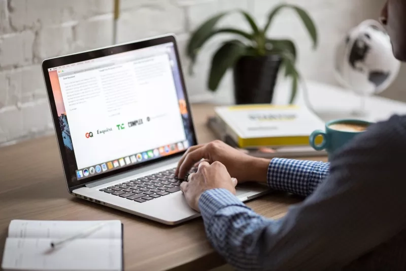 Person typing on laptop in office with notebook, pen, coffee, and globe on desk.