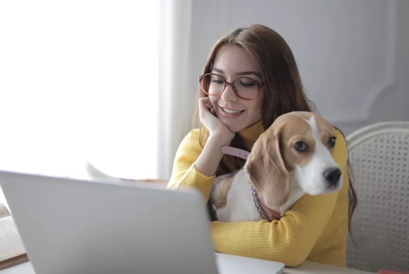 Woman working at home with a dog on her lap, smiling at the camera.