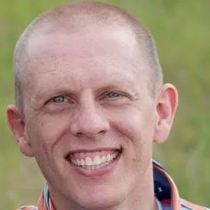 Close up headshot of Michael Sorensen smiling, wearing an orange and blue shirt, and standing in a field.