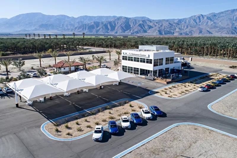 An aerial view of BMW Performance Center with cars, white canopy, mountain, and building with text.