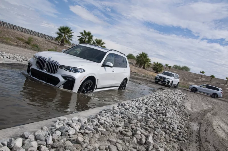 A BMW X5 driving through water with other BMWs following behind in the desert.
