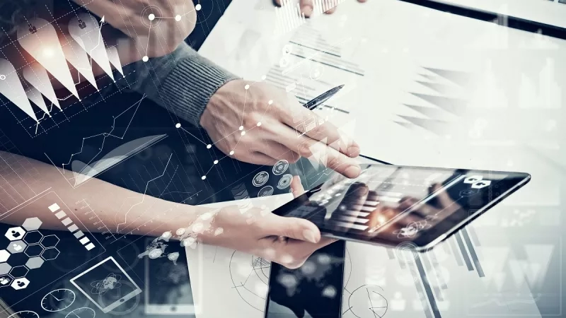 A person using tablet with pen and paper in front of him, with graphs and charts.