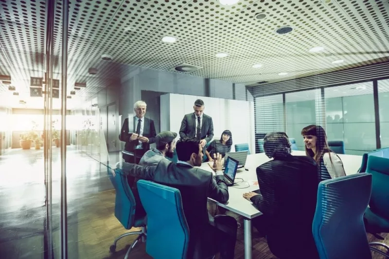 A group of people are gathered in a meeting room, discussing the need for conference management.