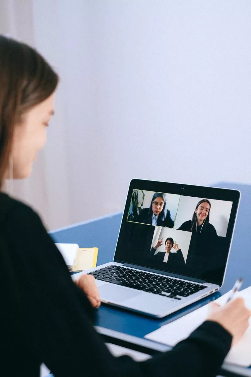 A woman is sitting at a desk and looking at a laptop with three people on it.